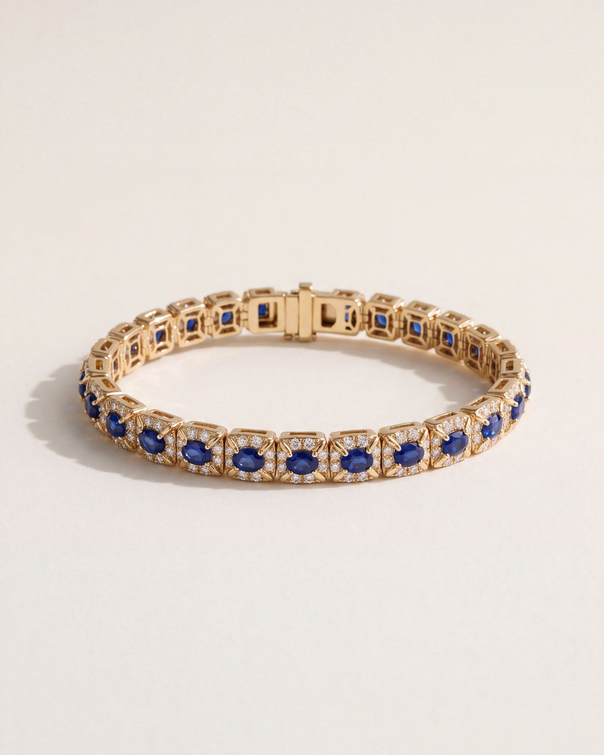 Oval Sapphire Halo Bracelet in 18k yellow gold, oval blue sapphires in leaf-shaped claws, each circled by eight round diamonds