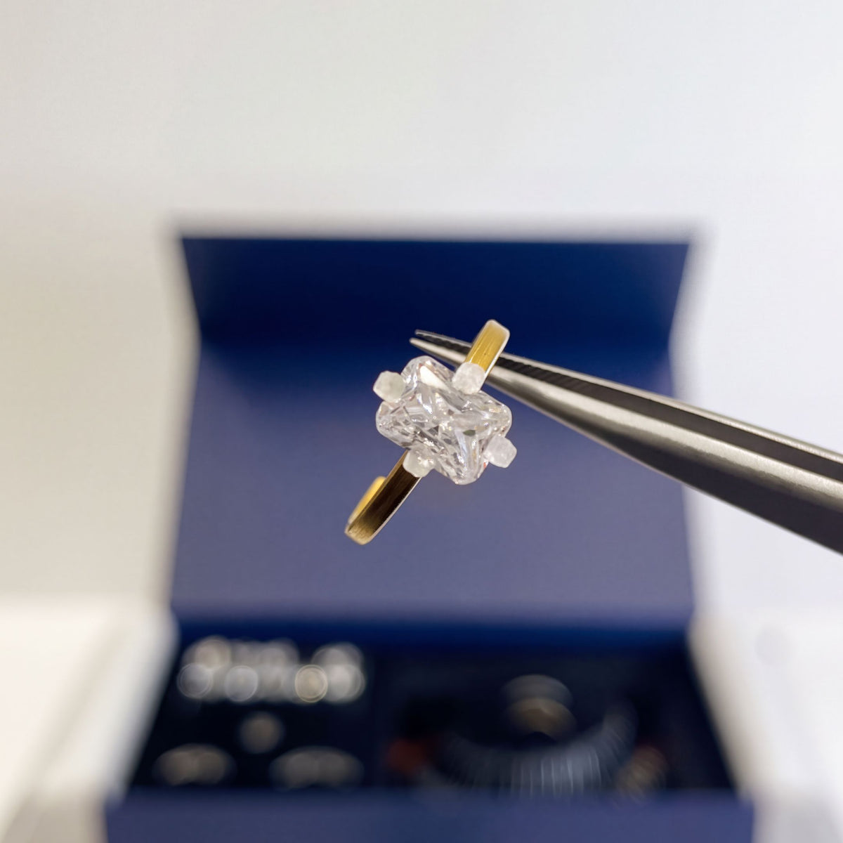 A radiant-shaped try-on stone held in tweezers above the open kit