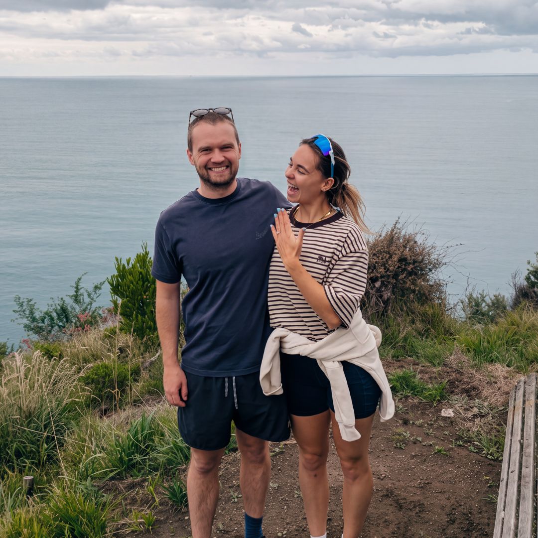 A newly engaged couple on a clifftop above the sea, showing their Henry Francis engagement ring