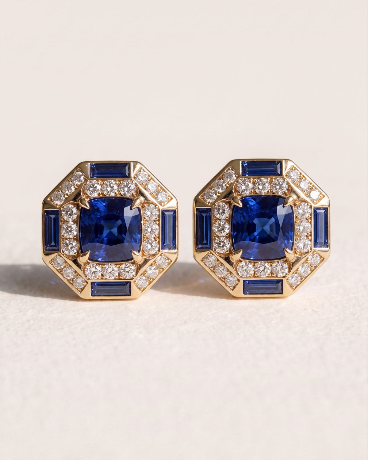 Octagon Sapphire Halo Studs in 18k yellow gold, a cushion blue sapphire framed by round diamonds and sapphire baguettes in an eight-sided border