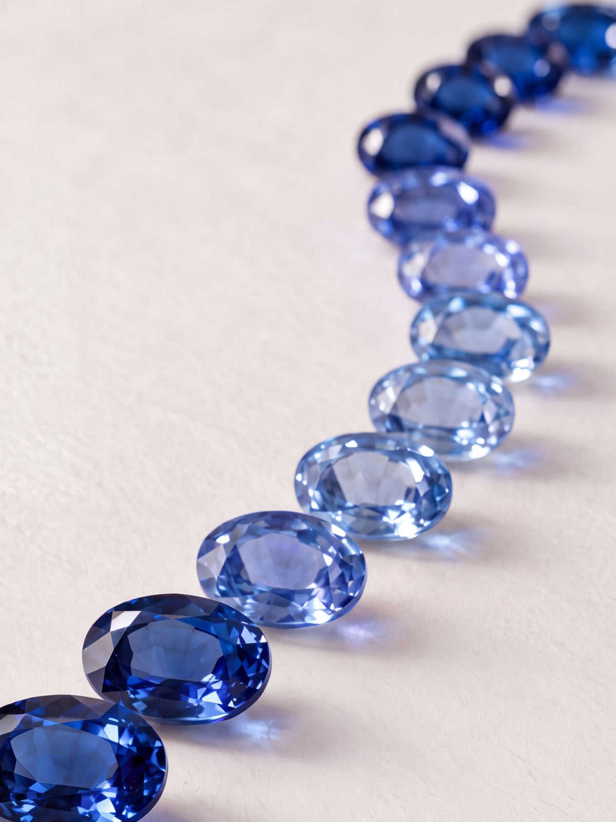 A curved row of oval blue sapphires laid out from light to deep blue for color matching