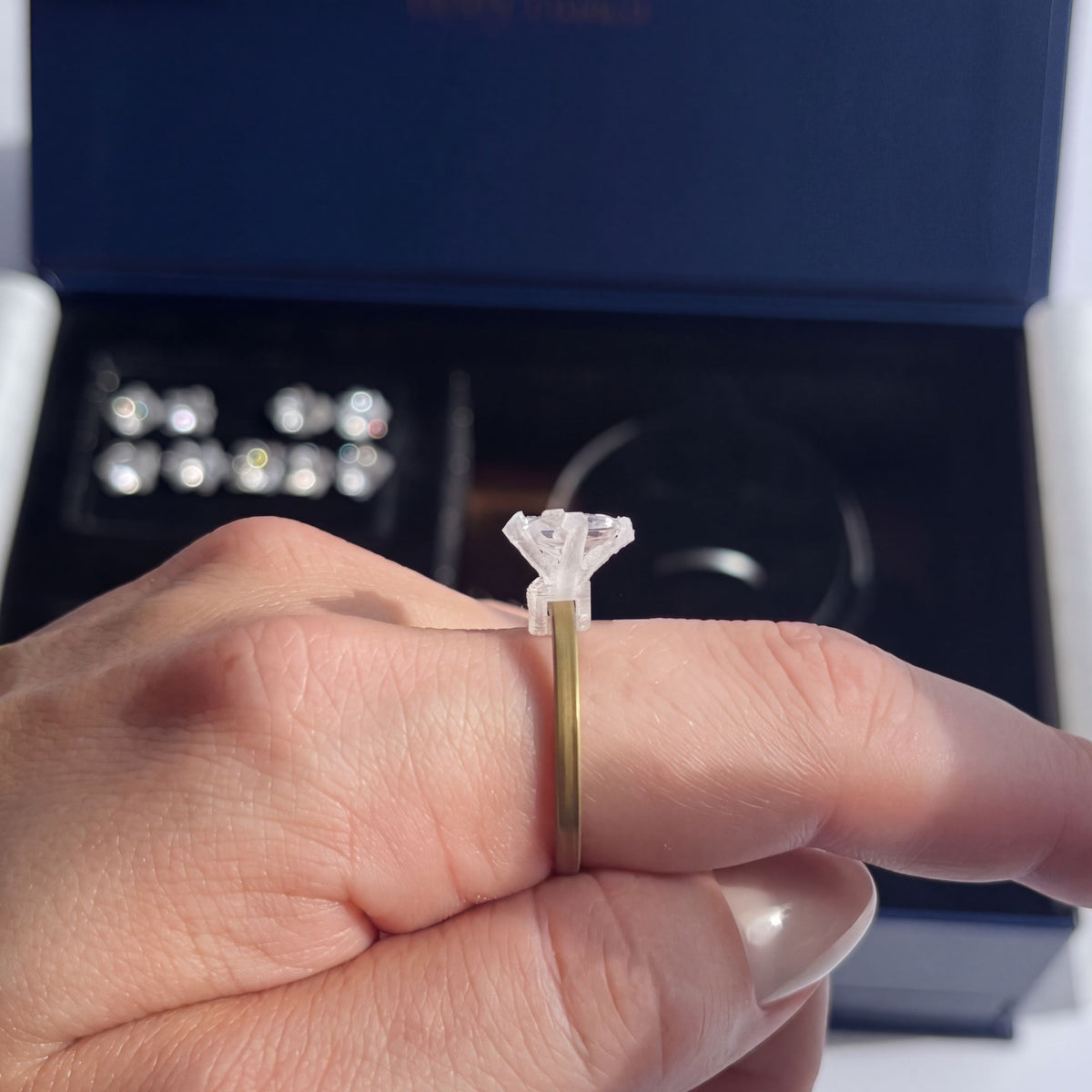 A try-on stone on a gold band worn on the hand, with the kit open behind