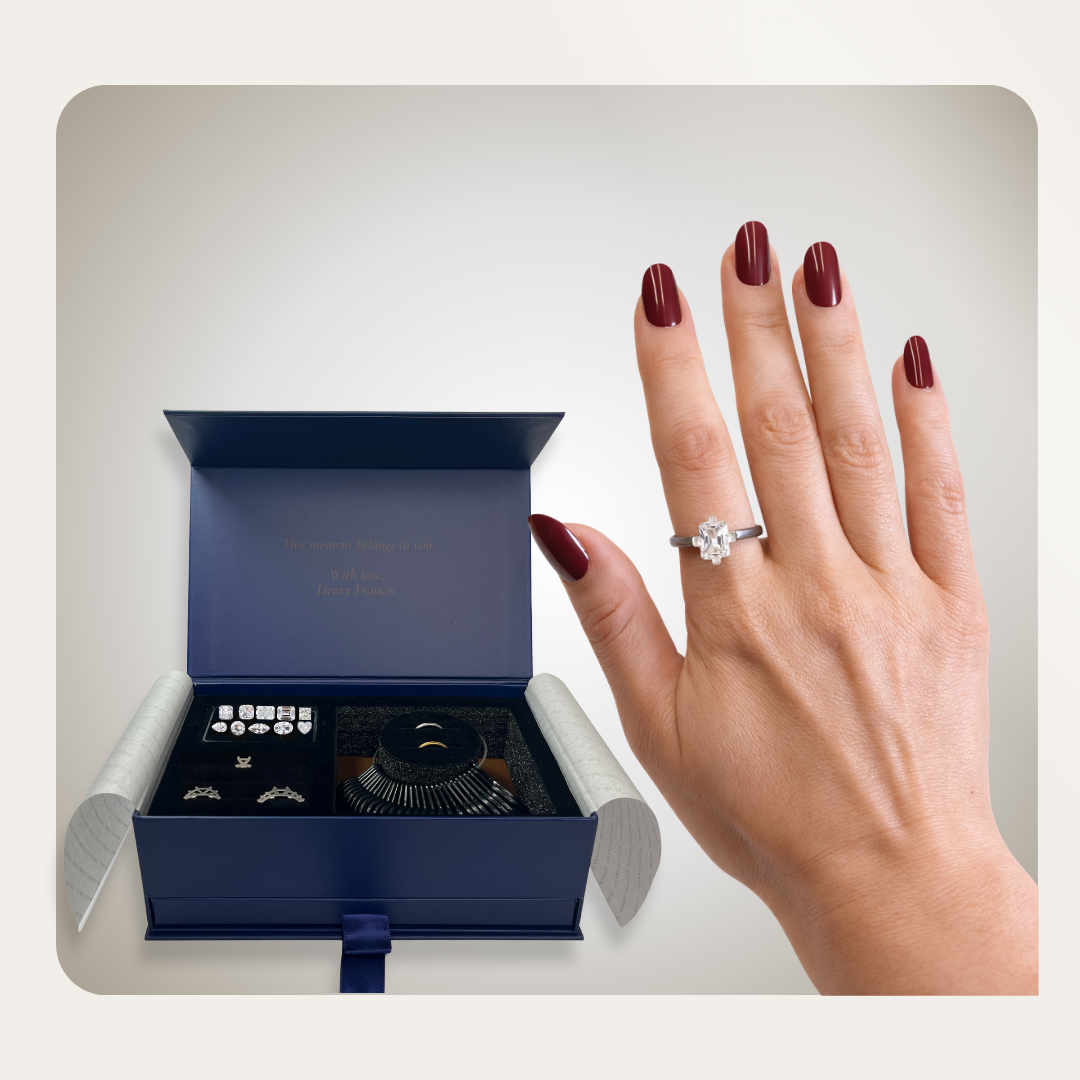 Hand wearing emerald-cut ring beside open navy Henry Francis try-on kit with stone replicas, two-tone bands, and sizing tool